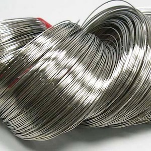 May include: A bundle of shiny, silver-colored wire, tightly coiled and bound with a red band. The wire appears to be made of a metallic material, reflecting light and creating a bright, clean appearance. The wire is likely used for crafting or jewelry making.