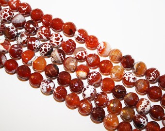 May include: Strands of faceted, round beads in shades of red, orange, and brown with white patterned accents. The beads are strung together, creating a textured and colorful display, perfect for jewelry making.