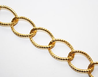 May include: Close-up of a gold-colored chain with oval links. The links have a textured, hammered appearance. The chain is set against a white background, highlighting its metallic sheen. This jewelry piece is suitable for necklaces or bracelets.
