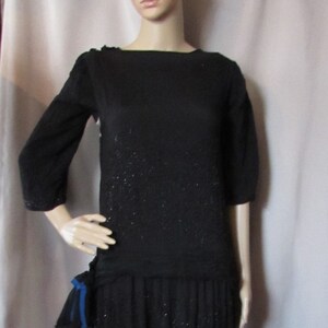 May include: A black beaded dress with a blue ribbon accent. The dress has a scoop neckline and 3/4 sleeves.