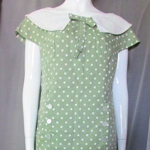 May include: A green dress with white polka dots and a white collar. The dress has a bow at the neckline and buttons down the front.