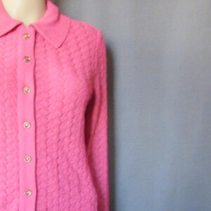 May include: A pink knitted cardigan with a collared neckline and button closure, paired with a matching pink pleated skirt.