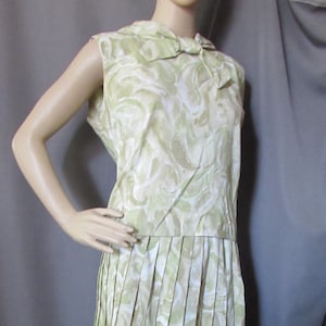 May include: A sleeveless dress with a pleated skirt. The dress is made of a light green and white fabric with a swirling pattern. The dress has a bow at the neckline.