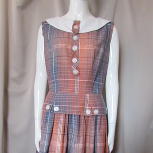 May include: A sleeveless dress with a plaid pattern in shades of blue, orange, and white. The dress has a white collar and a row of white buttons down the front.