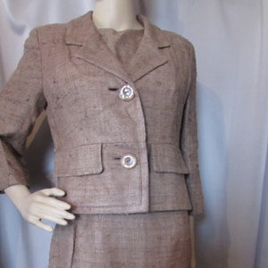 May include: A brown linen suit with a jacket and skirt. The jacket has a notched collar, two button closures, and two flap pockets. The skirt is knee-length and has a straight silhouette.