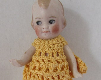 Tiny bisque doll with painted features Curled forelock hair blonde tone, eyes deep blue, cheeks and lips are pink. Arms strung,
