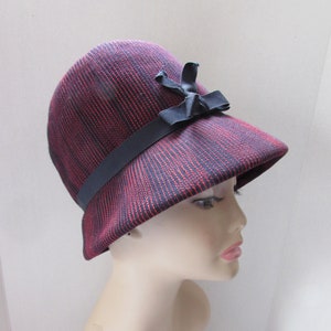 Op de afbeelding: Een rood-zwarte gestreepte cloche-hoed met een zwart lint en strik.