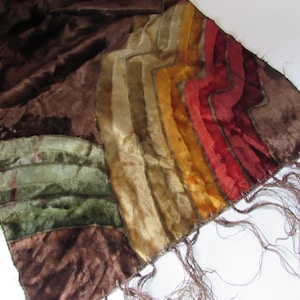 May include: A brown velvet scarf with a colorful striped design. The scarf features sections of green, gold, orange, and red stripes. The scarf has a fringed edge.