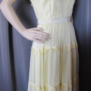 May include: A pale yellow, floor-length dress with a lace trim and a satin sash. The dress has a ruffled neckline and short sleeves.