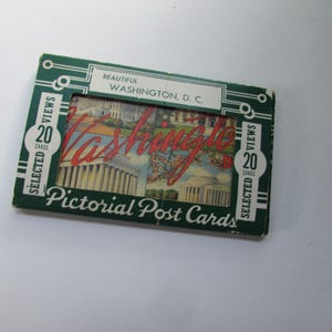 May include: A vintage green box of "Pictorial Post Cards" featuring 20 selected views of Washington, D.C. The box has a white and red design with the word "Washington" in a cursive font. The box is on a white surface.
