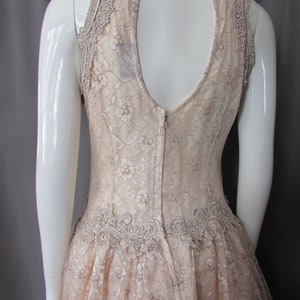 May include: A blush-colored lace dress with a keyhole back and a scalloped lace trim. The dress has a fitted bodice and a full skirt.