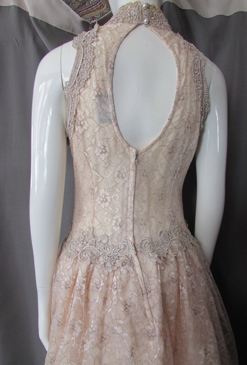 May include: A blush-colored lace dress with a keyhole back and a scalloped lace trim. The dress has a fitted bodice and a full skirt.