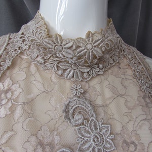 May include: A close-up of a beige lace halter top with a high neckline. The lace is delicate and features a floral pattern.