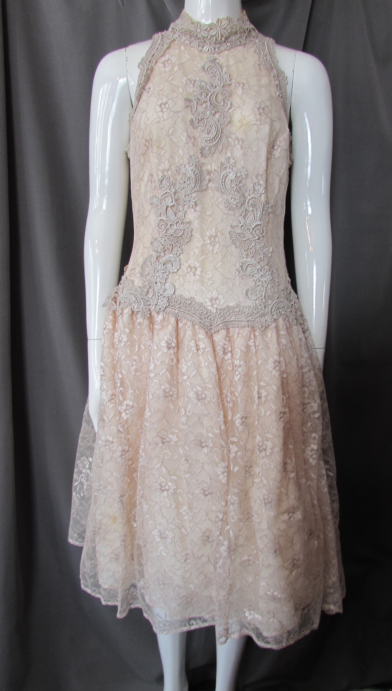 May include: A pale pink lace dress with a high neckline and a full skirt. The dress is decorated with delicate floral lace.