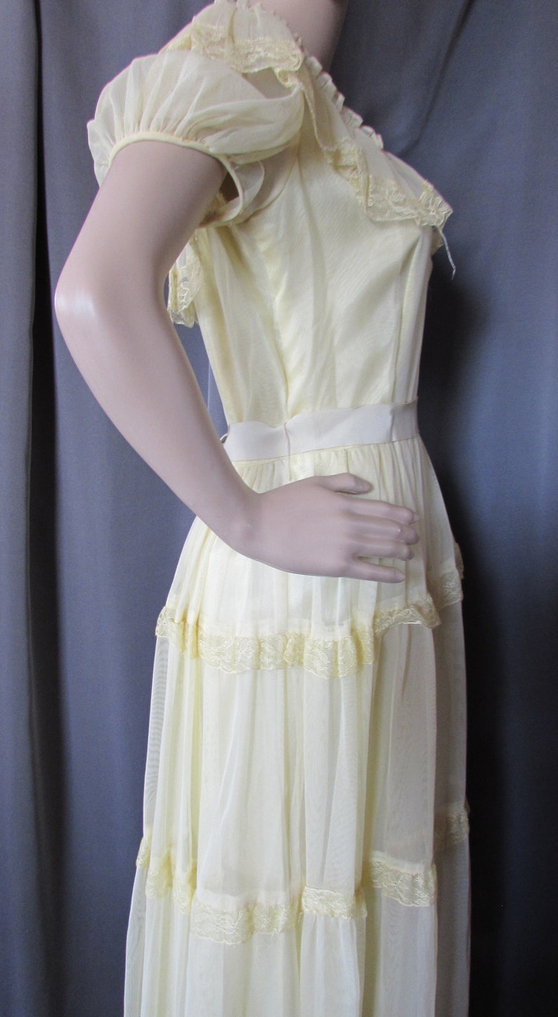 May include: A pale yellow, tiered maxi dress with lace trim and puff sleeves. The dress is made of a sheer fabric and has a fitted bodice.