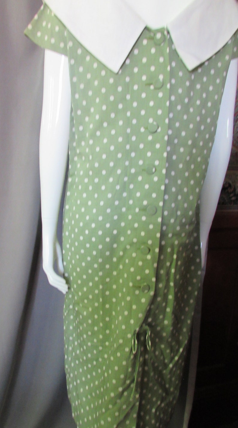 May include: A green dress with white polka dots and a white collar. The dress has a button-up front and a tie at the waist.