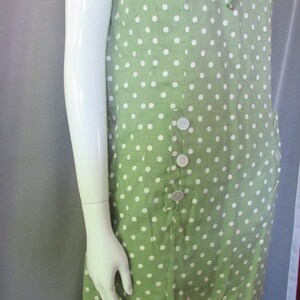 May include: A green dress with white polka dots and a white collar. The dress has a bow at the neckline and buttons down the front.