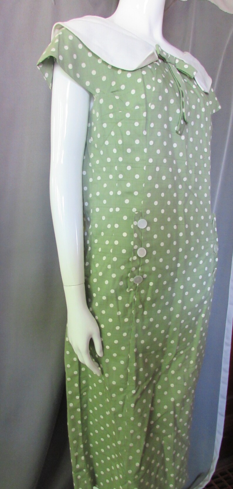May include: A green dress with white polka dots and a white collar. The dress has a bow at the neckline and buttons down the front.