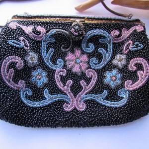 Puede incluir: Un bolso de noche negro de cuentas con un diseño floral en rosa, azul y plateado. El bolso tiene un cierre de broche y una correa de cadena.