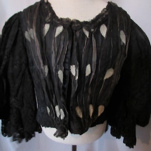 May include: A black silk blouse with a lace trim and silver leaf embroidery. The blouse has a gathered neckline and puffed sleeves.