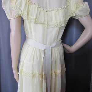 May include: A pale yellow, tiered maxi dress with a lace trim and a white sash. The dress has a sheer, ruffled neckline and short sleeves.