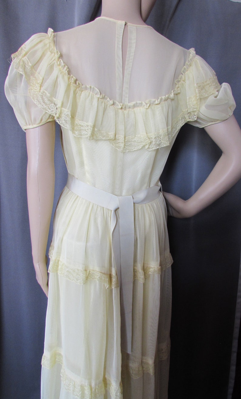 May include: A pale yellow, tiered maxi dress with a lace trim and a white sash. The dress has a sheer, ruffled neckline and short sleeves.
