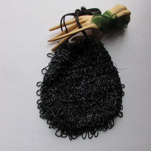 May include: A black beaded evening bag with a fringe detail. The bag is hanging from a wooden hand with a green ribbon.