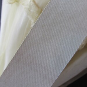 May include: Close-up of a white satin ribbon with a textured surface.