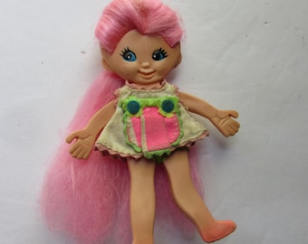 May include: A vintage plastic doll with pink hair, blue eyes, and a light green and pink dress. The doll has a smiling face and is wearing a dress with an owl design.