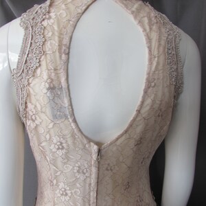 May include: A sleeveless, nude lace dress with a keyhole back and a zipper closure. The dress has a delicate floral pattern and a scalloped hem.