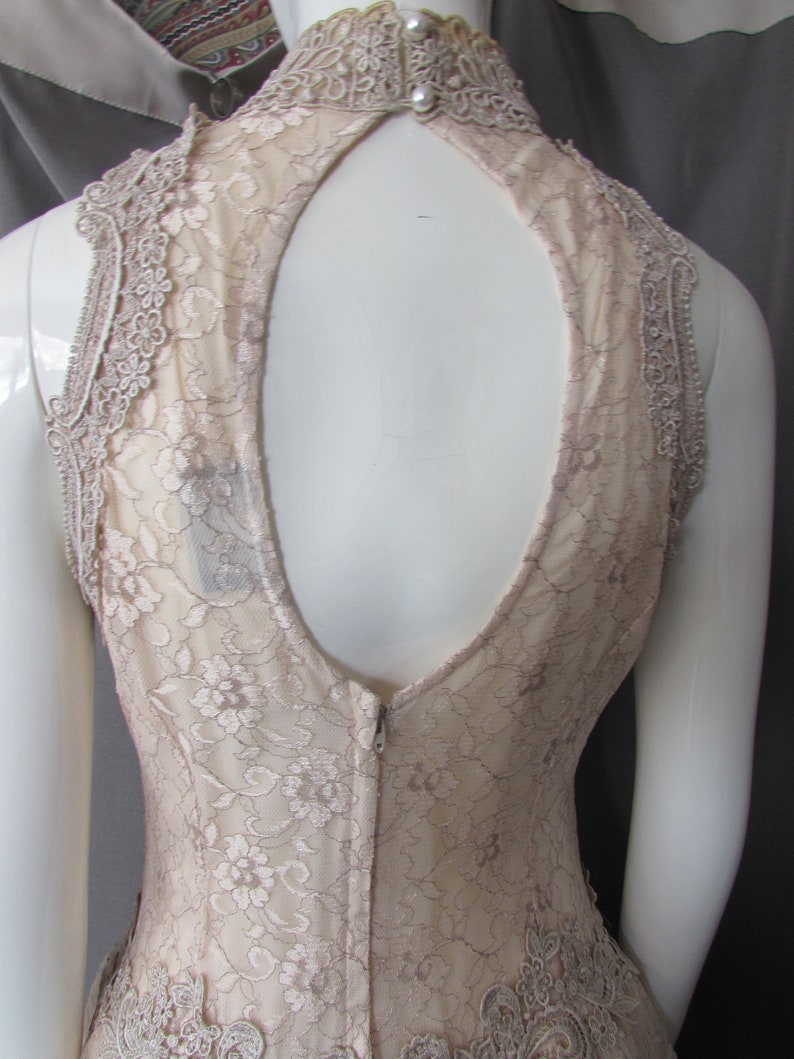 May include: A sleeveless, nude lace dress with a keyhole back and a zipper closure. The dress has a delicate floral pattern and a scalloped hem.