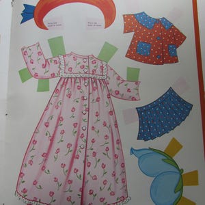May include: A vintage paper doll page featuring cut-out clothing and accessories. The clothing includes a pink floral nightgown, a red polka-dot top, a blue skirt with white dots, and a blue flower. An orange hat with a blue bow is also included.