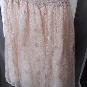 May include: A beige lace dress with a scalloped lace trim at the top. The dress has a flowy, A-line silhouette.