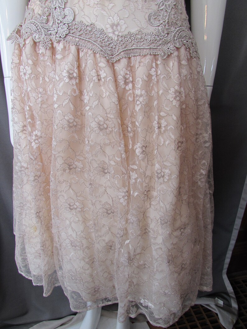 May include: A beige lace dress with a scalloped lace trim at the top. The dress has a flowy, A-line silhouette.