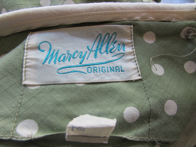 May include: A white label with blue embroidered text that reads "Marcy Allen Original" on a green fabric with white polka dots.