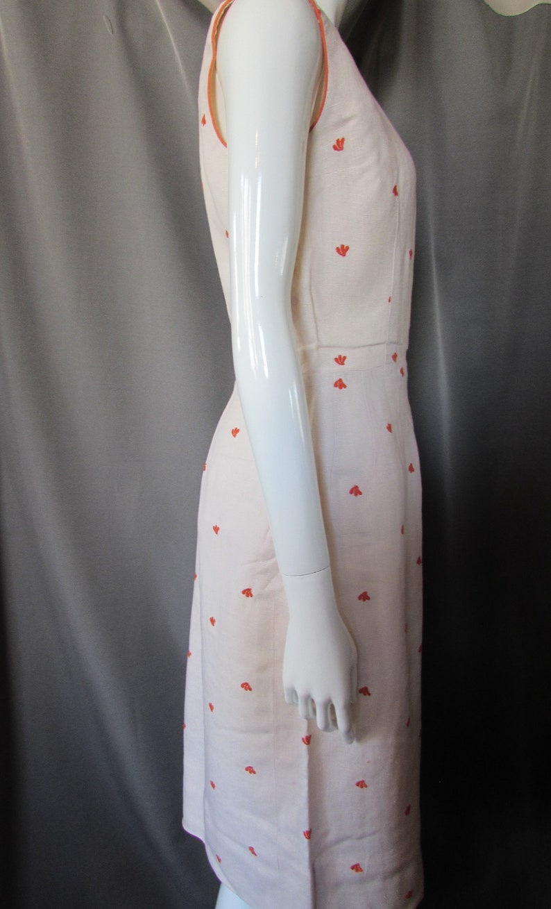 May include: A sleeveless white dress with a red floral pattern. The dress has a scoop neck and a fitted bodice. The dress is made of a lightweight fabric and is perfect for summer.