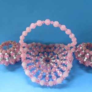 May include: A pink beaded basket with a handle and two matching smaller baskets. The baskets are made of safety pins and beads.