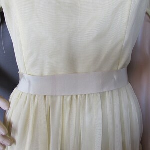 May include: A pale yellow dress with a white satin sash. The dress has a gathered skirt and short sleeves.