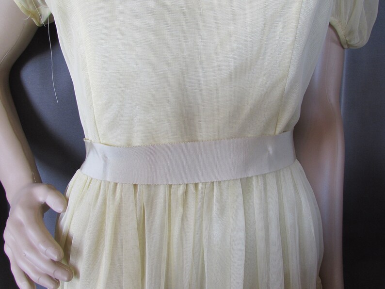 May include: A pale yellow dress with a white satin sash. The dress has a gathered skirt and short sleeves.