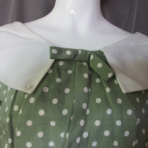 May include: A green dress with white polka dots and a white collar. The dress has a bow at the neckline.