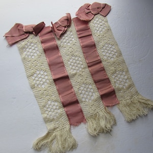 May include: Four vintage lace panels with pink ribbon accents and bows. The panels are cream-colored with a diamond-shaped openwork design. Each panel has a pink ribbon stripe down the center and a fringe at the bottom. The top of each panel has a pink bow.
