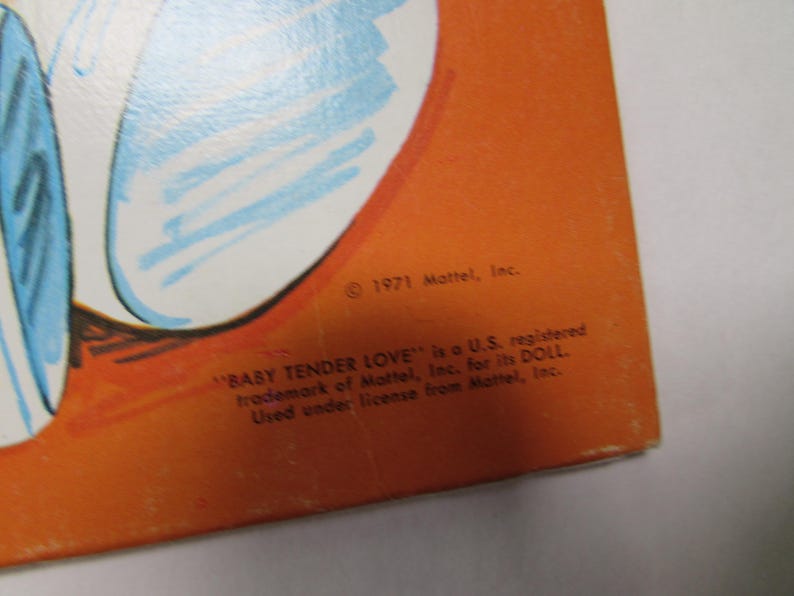 May include: An orange background with a partial illustration in blue and white. The text reads "&copy; 1971 Mattel, Inc." and "BABY TENDER LOVE" is a U.S. registered trademark of Mattel, Inc. for its DOLL. Used under license from Mattel, Inc."