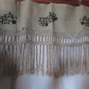 May include: Tan valance with embroidered green leaves and red berries. The valance has a crocheted trim and fringe. The design is repeated across the top of the valance. The valance is hanging in front of a white curtain.