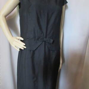 Puede incluir: Un vestido negro sin mangas con un lazo en la cintura. El vestido est&aacute; hecho de una tela lisa y tiene un dise&ntilde;o simple y elegante.