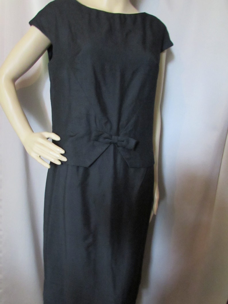 Puede incluir: Un vestido negro sin mangas con un lazo en la cintura. El vestido est&aacute; hecho de una tela lisa y tiene un dise&ntilde;o simple y elegante.