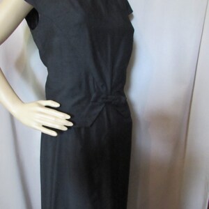 Puede incluir: Un vestido negro sin mangas con un lazo en la cintura.