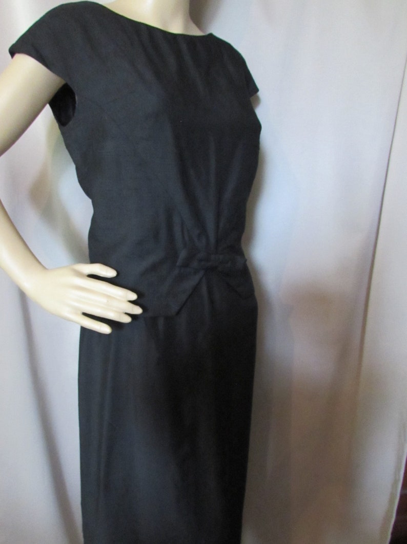Puede incluir: Un vestido negro sin mangas con un lazo en la cintura.