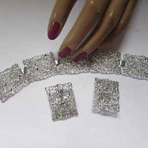 May include: A silver-toned jewelry set featuring a bracelet and matching earrings. The bracelet is composed of rectangular openwork links, and the earrings have a similar design. The set is displayed on a white surface.