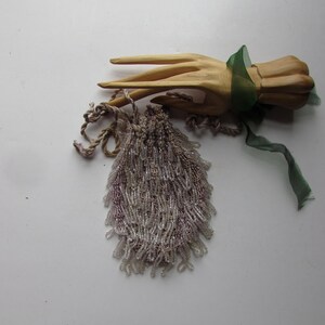 May include: A wooden hand sculpture with three extended fingers, tied with a green ribbon. A beaded purse with silver and pink beads is next to the sculpture. The purse has a drawstring closure and a tassel.