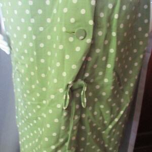 May include: A green dress with white polka dots and a tie at the waist. The dress has three buttons on the front.